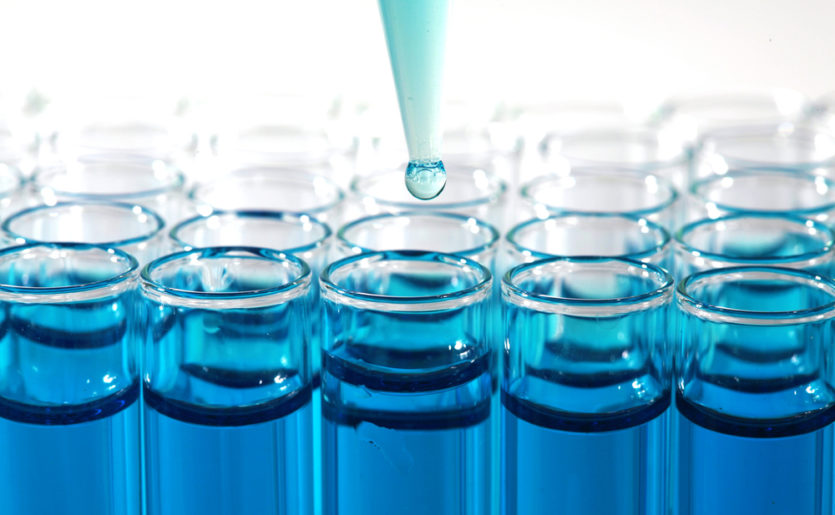 Close-up of a dropper putting blue liquid into a series of vials