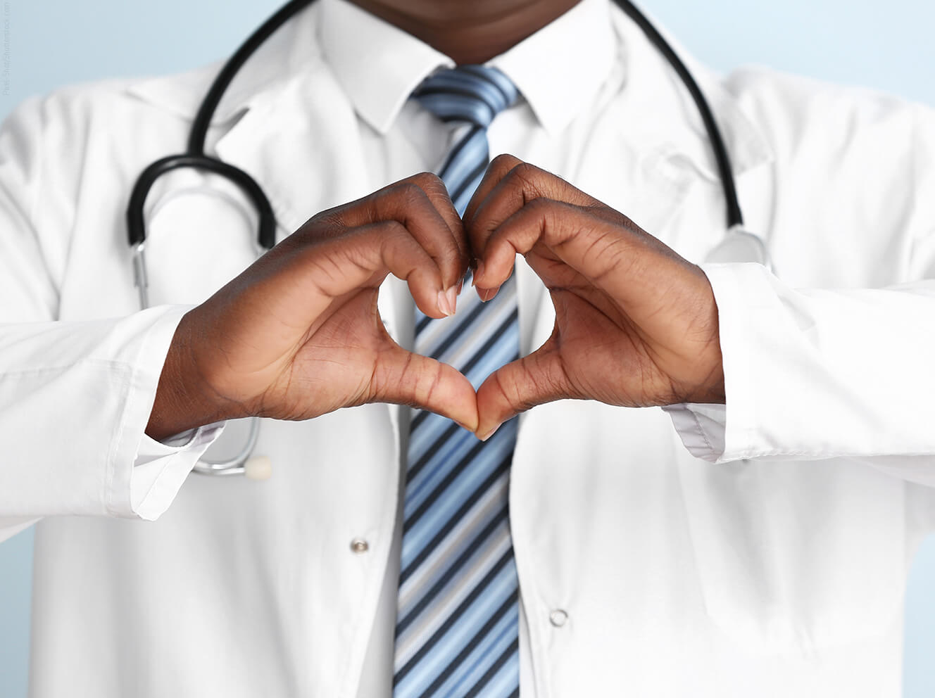 Close-up of a Black physician in a lab coat forming a heart shape with their hands
