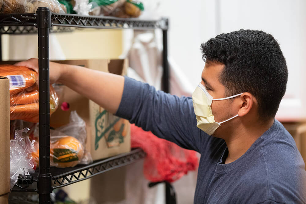 Man wearing mask restocking shelves at Mass General food pantry