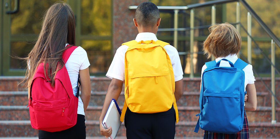 Three kids with colorful backpacks on their way to school